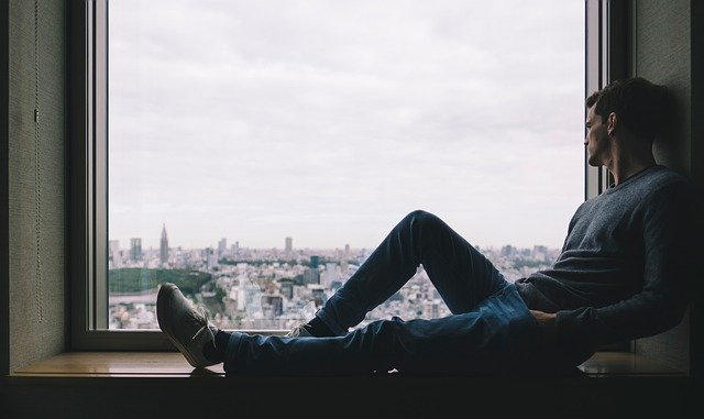 Muž sediaci pri okne s výhľadom na mesto.jpg